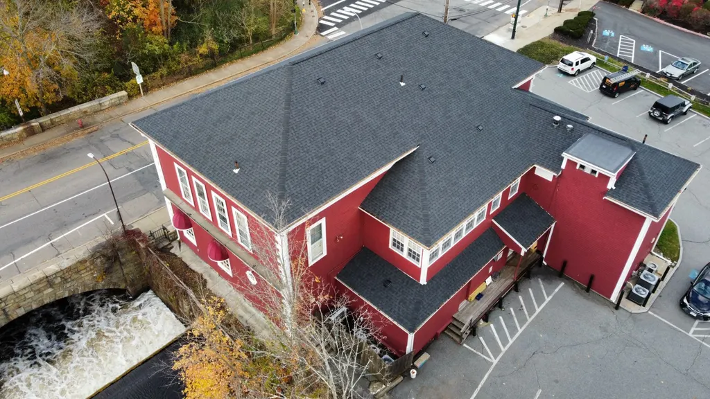 Aerial view of a red clapboard mill building beside a waterfall after a full re-roof