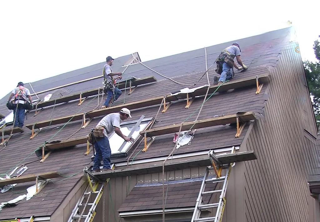 Newton Roofing crew on roof staging setting a new skylight into a steep shingle roof