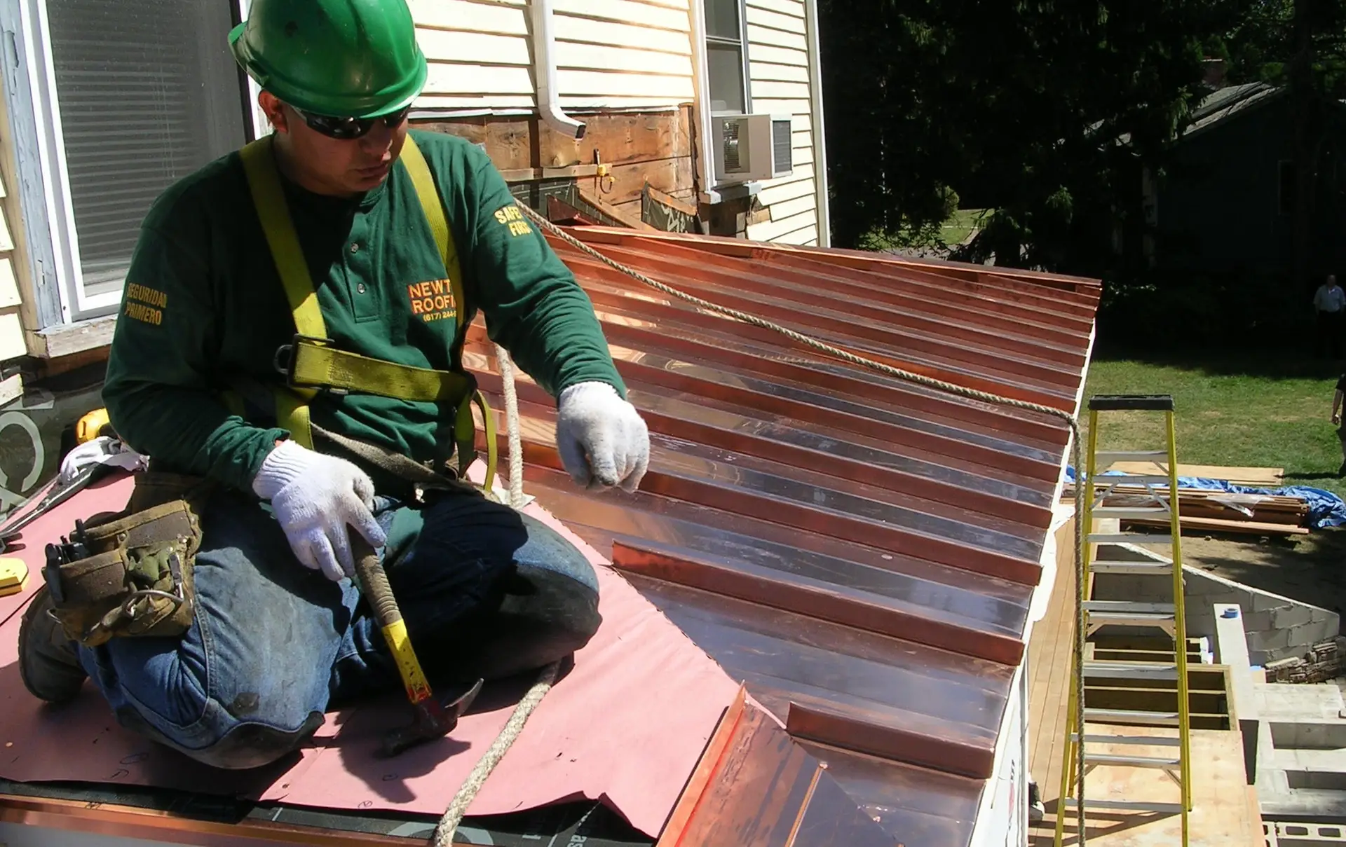 Newton Roofing crew member in a branded shirt setting standing seam copper panels on a bay roof