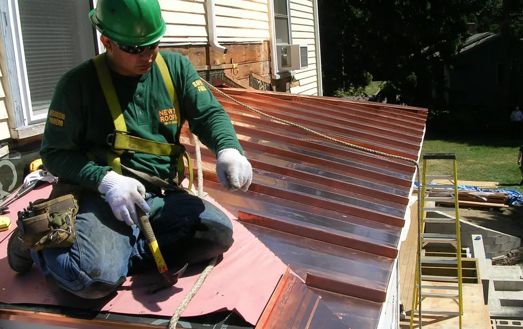 Newton Roofing crew member in a branded shirt setting standing seam copper panels on a bay roof