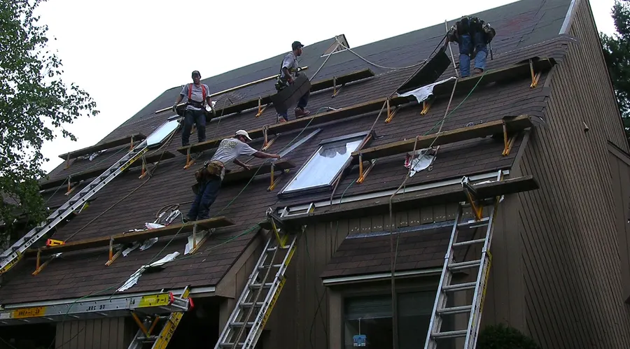 Four-person crew on roof staging stripping shingles from a steep pitched roof