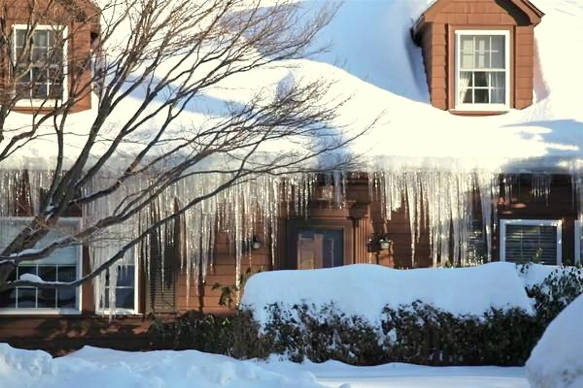 Heavy icicles and an ice dam hanging from the eaves of a snow-covered Boston-area house