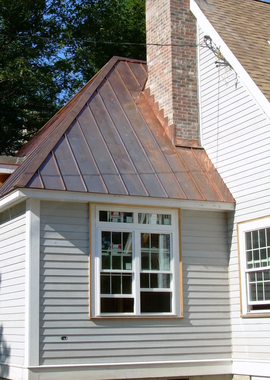 Newly installed standing seam copper dormer roof stepped into a brick chimney
