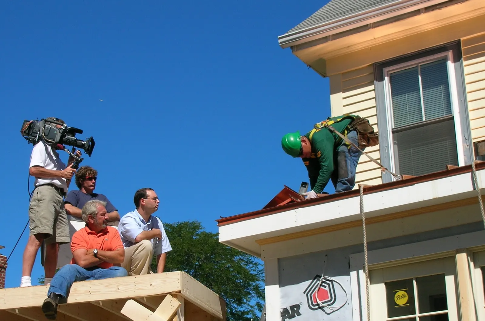 A television camera crew on staging filming a Newton Roofing crew member fitting copper along a porch roof