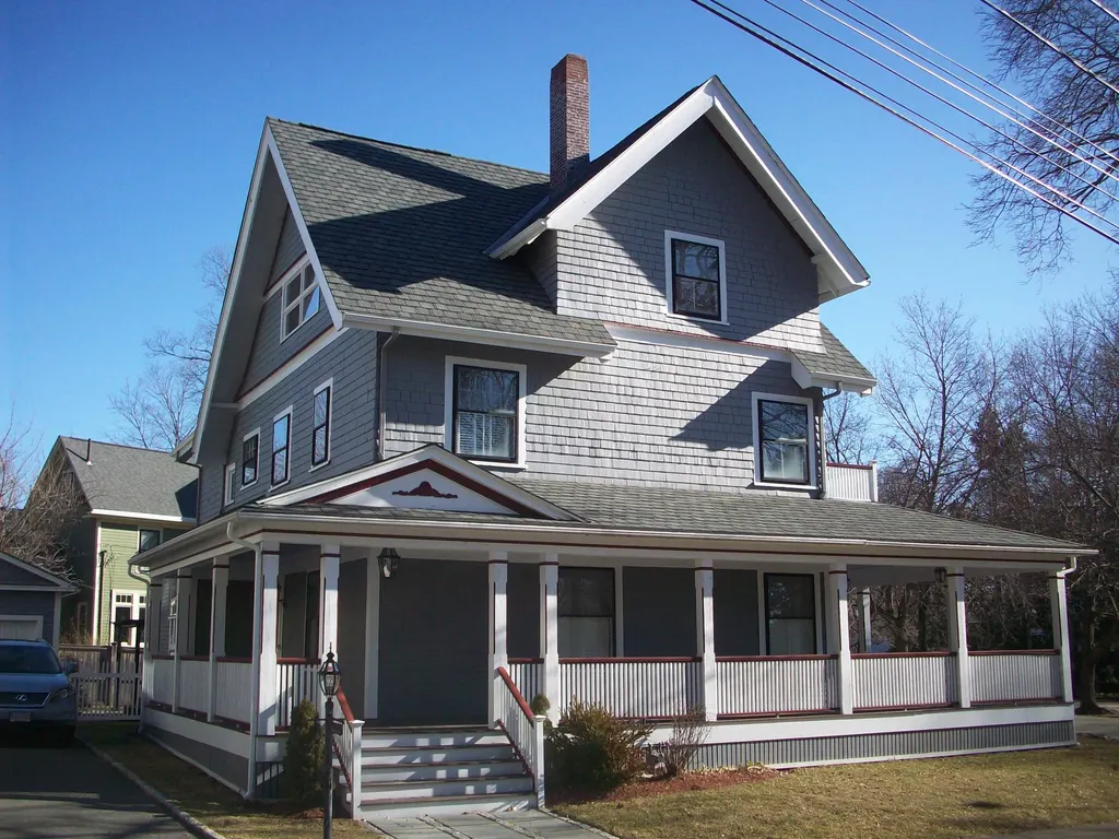 Gray shingle-style Victorian with a wraparound porch and freshly rebuilt trim and roofline